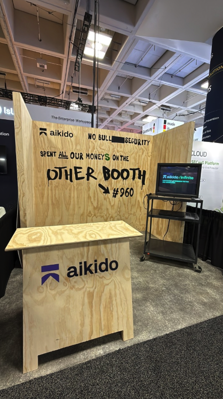 Aikido's 2026 RSAC decoy booth: a plywood stand with hand-painted copy reading 'NO BULL[REDACTED] SECURITY · SPENT ALL OUR MONEYS ON THE OTHER BOOTH → #960'.